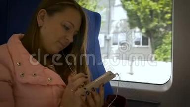 年轻的美女坐在火车上，用白色耳机听智能手机里的音乐